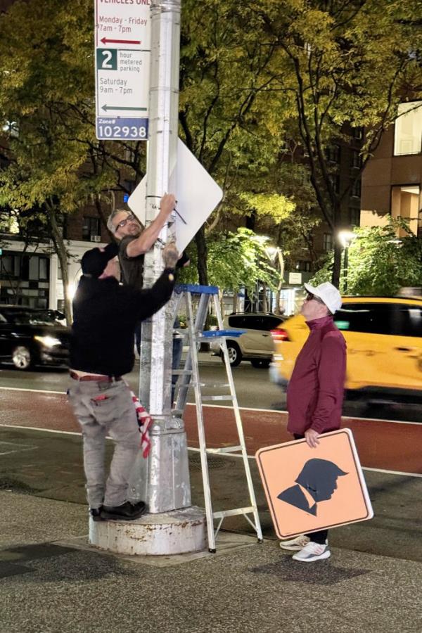 Artist Scott Lobaido hanging traffic signs featuring Do<em></em>nald Trump's profile with two men assisting him